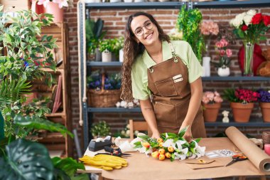 Young beautiful hispanic woman florist make bouquet of flowers at flower shop