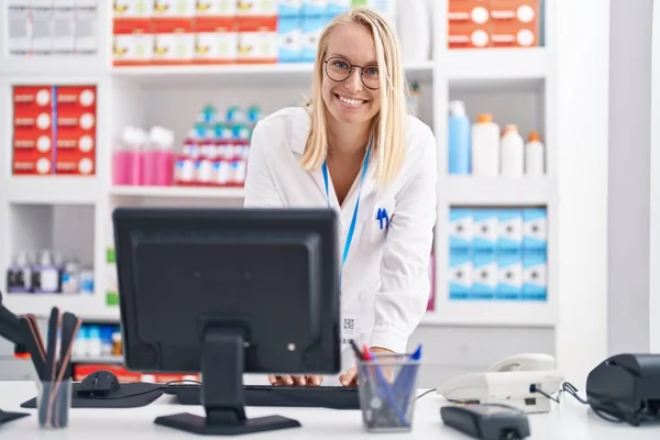 Young blonde woman pharmacist using computer working at pharmacy