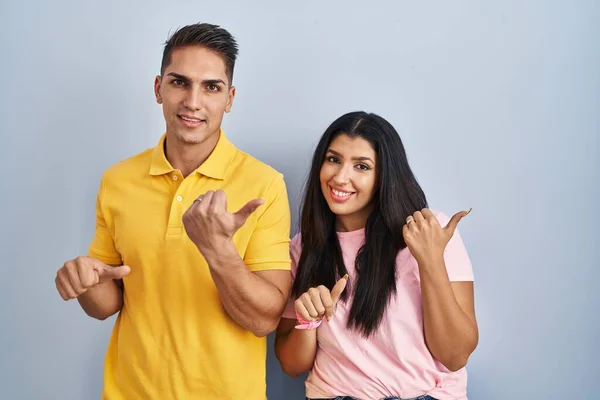 Young Couple Standing Isolated Background Pointing Back Hand Thumbs Smiling — Stock Photo, Image