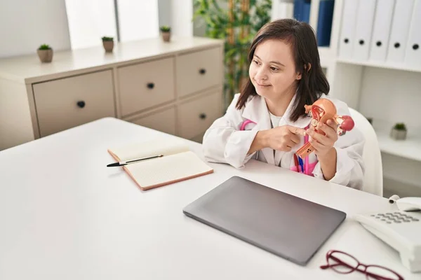 Down syndrome woman wearing doctor uniform holding anatomical model of uterus at clinic