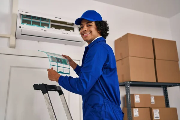 Young hispanic man technician repairing air conditioning at office