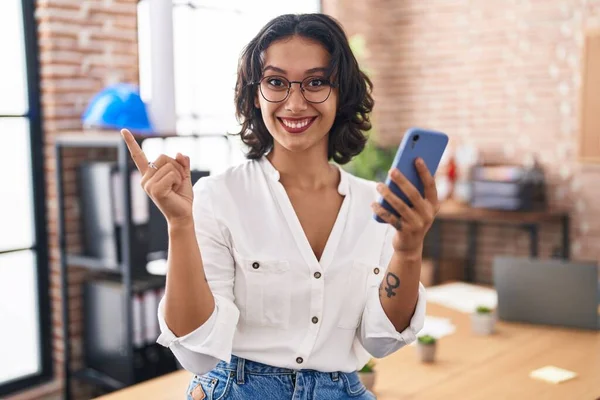 Mladá Hispánka Pracující Kanceláři Pomocí Smartphonu Šťastně Usmívá Ukazujíc Rukou — Stock fotografie