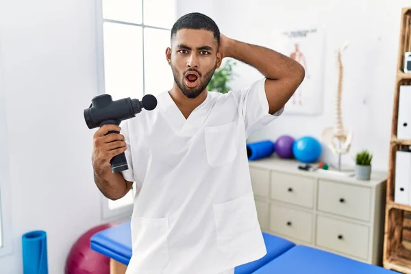 Young Indian Physiotherapist Holding Therapy Massage Gun Wellness Center Crazy — Stockfoto