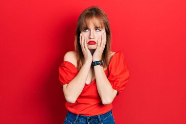 Kırmızı tişört giyen kızıl saçlı genç bir kadın. Yorgun eller, yüzü, depresyonu ve üzüntüyü örten, sorun yüzünden üzgün ve sinirli. 