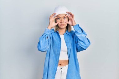 Beautiful blonde woman wearing wool hat trying to open eyes with fingers, sleepy and tired for morning fatigue 