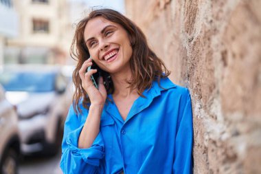 Gülümseyen genç bir kadın caddedeki akıllı telefondan konuşuyor.