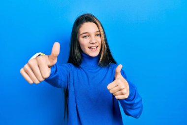 Young brunette girl wearing turtleneck sweater approving doing positive gesture with hand, thumbs up smiling and happy for success. winner gesture. 