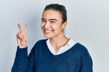 Gündelik kıyafetler giyen genç beyaz kız iki numarayı gösterip işaret ederken kendinden emin ve mutlu bir şekilde gülümsüyor.. 