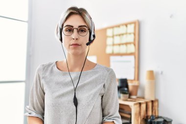 Young beautiful woman working at the office wearing operator headset thinking attitude and sober expression looking self confident 