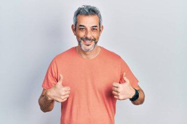 Gri saçlı, sıradan tişörtlü, yakışıklı, orta yaşlı bir adam. Başarı işareti yapıyor. Elleriyle olumlu jest yapıyor. Neşeli ifade ve kazanan jest. 