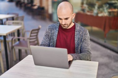 Genç adam kahve dükkanının terasında dizüstü bilgisayar kullanıyor.