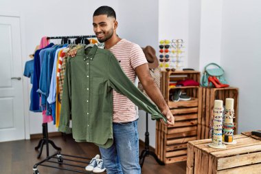 Young arab man holding shirt shopping at clothing store