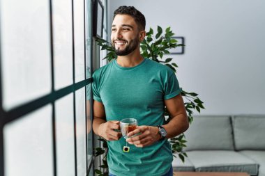 Genç Arap adam evde çay içerek kendinden emin gülümsüyor.