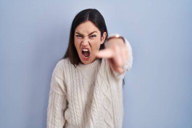 Genç esmer kadın mavi arka planda dikiliyor. Kameraya kızgın ve sinirli olduğunu gösteriyor. 