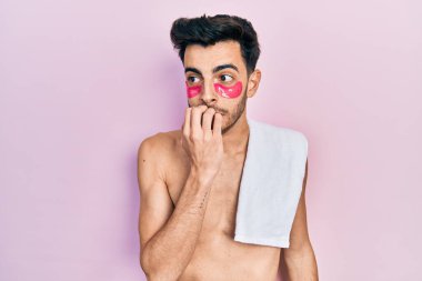 Havlu ve göz torbaları takan İspanyol asıllı genç adam elleri ağız yiyen tırnaklarla gergin ve stresli görünüyor. anksiyete. 