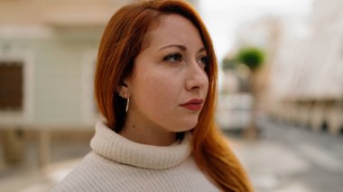 Sokakta ciddi bir ifadeyle duran genç kızıl saçlı kadın.