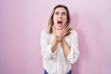 Young beautiful woman standing over pink background shouting suffocate because painful strangle. health problem. asphyxiate and suicide concept. 