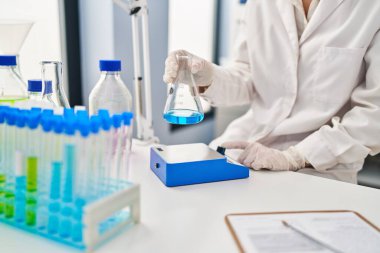 Young caucasian woman wearing scientist uniform measuring liquid at laboratory