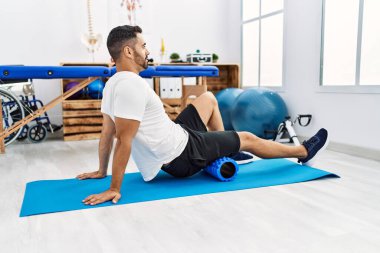 Genç İspanyol hasta klinikte köpük silindir kullanarak bacak rehabilitasyonu seansı yapıyor.