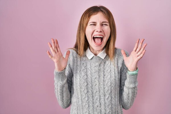 Красивая женщина стоит на розовом фоне празднует сумасшедший и поражен успехом с поднятыми руками и открытыми глазами, крича взволнован. победитель концепция 