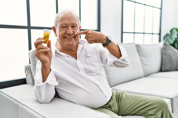 Senior Man Holding Pills Pointing Hand Finger Face Nose Smiling — Stock fotografie
