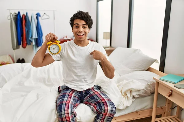 Junger Hispanischer Mann Mit Wecker Sitzt Schlafzimmer Und Zeigt Mit — Stockfoto