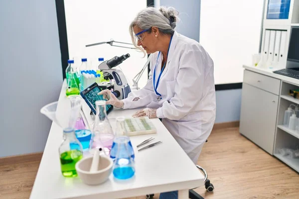中年妇女穿着科学家制服在实验室的触摸板上观察胚胎 — 图库照片