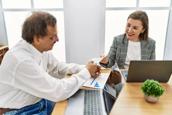 Middle age man and woman business workers using laptop paying dollars at office