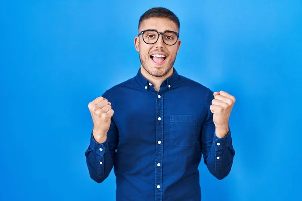 Jovem Hispânico Vestindo Óculos Sobre Fundo Azul Comemorando Surpreso Surpreso — Fotografia de Stock