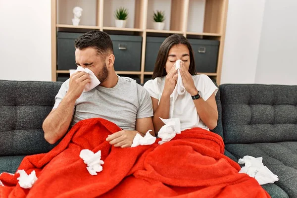 Young latin ill couple using napkin sititng on the sofa at home.