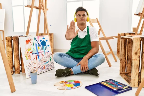 Young hispanic man at art studio doing stop sing with palm of the hand. warning expression with negative and serious gesture on the face.