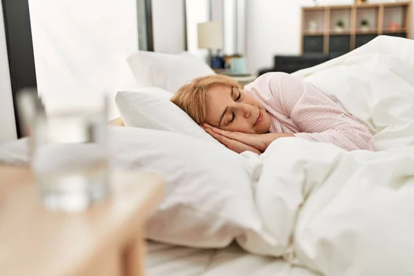 Middle age blonde woman sleeping on the bed at home.