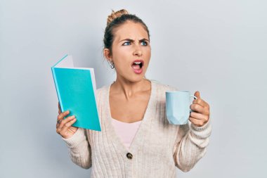 Sarışın, güzel, beyaz bir kadın kitap okuyor ve bir fincan kahve içiyor kızgın ve öfkeli çığlıklar atıyor ve öfkeyle bağırıyor. öfke ve agresif konsept. 