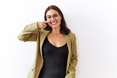 Genç esmer kadın izole edilmiş arka planda duruyor. Parmaklarıyla yüzünü ve burnunu işaret ediyor. Neşeli bir şekilde gülümsüyor. güzellik konsepti 