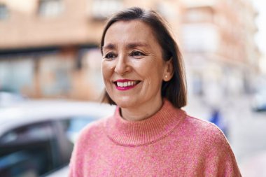 Orta yaşlı bir kadın sokakta kendine güvenerek gülümsüyor.