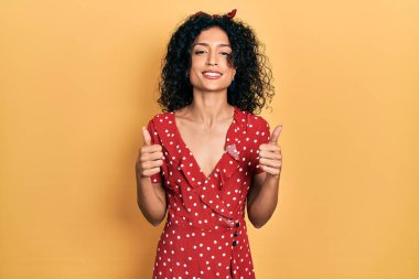 Yazlık elbise giyen genç Latin kız. Elleriyle olumlu jest yapıyor. Gülümsüyor ve mutlu. Neşeli ifade ve kazanan jest. 