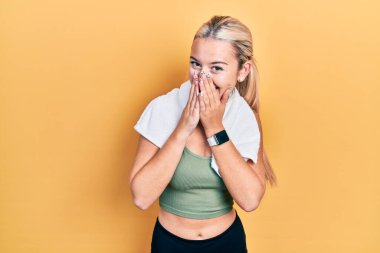 Spor kıyafetleri ve havlu giymiş genç sarışın kız gülüyor ve utanıyor kıkırdıyor ağızlarını ellerle kapatıyor, dedikodu ve skandal konsepti yapıyor. 