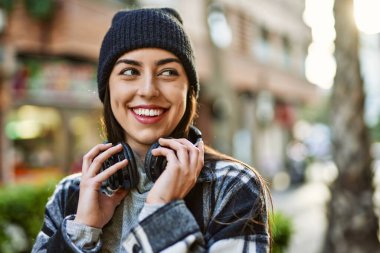 Genç İspanyol kadın şehirde kulaklık takarak mutlu gülümsüyor..
