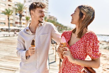 Genç İspanyol çift tatilde gülümseyerek kumsalda dondurma yiyor.