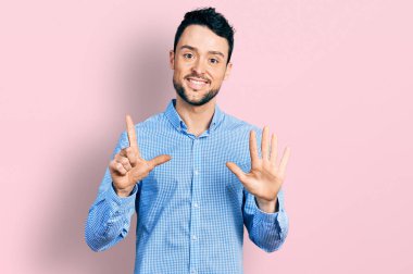 Sakallı, sıradan iş gömleği giyen İspanyol bir adam yedi numarayı gösterip işaret ederken kendine güvenen ve mutlu bir şekilde gülümsüyor.. 