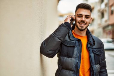 Yakışıklı, sakallı, mutlu, kendine güvenen, kışlık palto giymiş telefonda konuşan bir İspanyol.