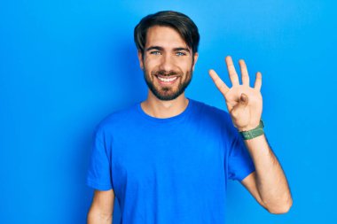 İspanyol asıllı genç adam, gündelik giysiler giyip dört numarayı gösterip işaret ederken kendinden emin ve mutlu bir şekilde gülümsüyor.. 
