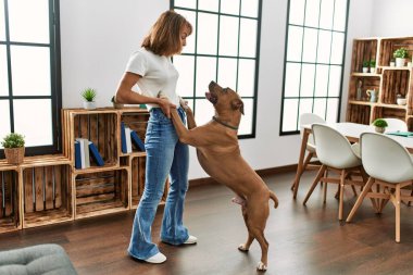 Beyaz bir kadın gülümseyerek evde köpekle dans ediyor.