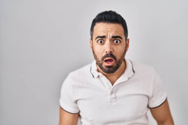 Young hispanic man with beard wearing casual clothes over white background afraid and shocked with surprise and amazed expression, fear and excited face. 