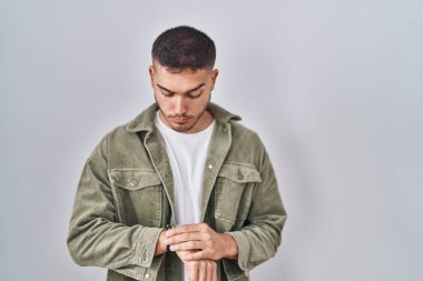 Tecrit edilmiş arka planda duran genç İspanyol adam saati kontrol ediyor, rahat ve kendinden emin. 