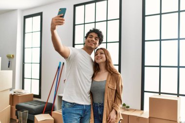 Young couple smiling happy making selfie by the smartphone at new home.