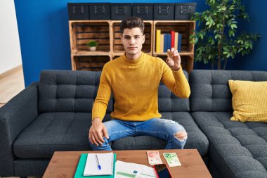 Young hispanic man holding bitcoin virtual money thinking attitude and sober expression looking self confident 