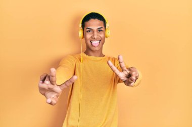 Genç Afro-Amerikalı adam müzik dinliyor kulaklıkla gülümsüyor ve iki elini de zafer işareti yaparken gösteriyor. İki numara.. 