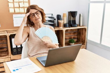 Middle age hispanic woman using handfan working at office
