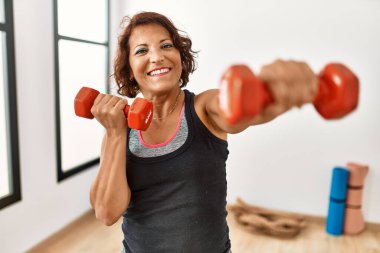 Orta yaşlı İspanyol sporcu kadın spor merkezinde dambıllar kullanarak mutlu bir antrenman yapıyor..